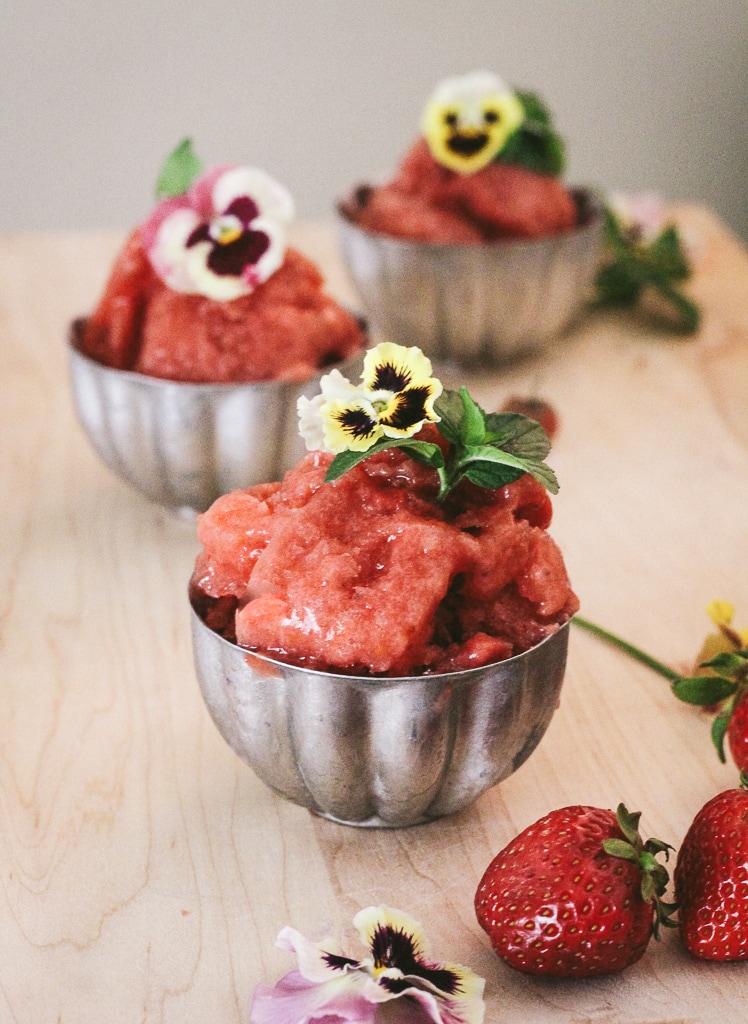 Front view of strawberry sorbet served in vintage jello molds garnished with pansies and mint leaves.